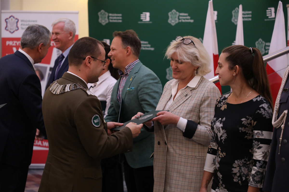 Fot. 4. Uczestniczka konferencji podczas wygłaszanej prezentacji. Osoba stoi przy mównicy, przodem do zgromadzonych siedzących na sali - auli.