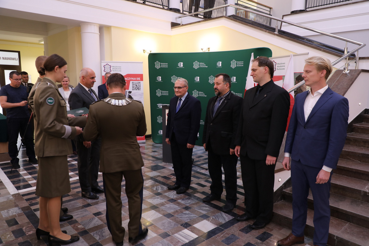 Fot. 5. Rektor-Komendant wraz z prorektorem ds. nauki wręczają nagrodę zespołowi naukowemu - 4 osoby stojace w szeregu.