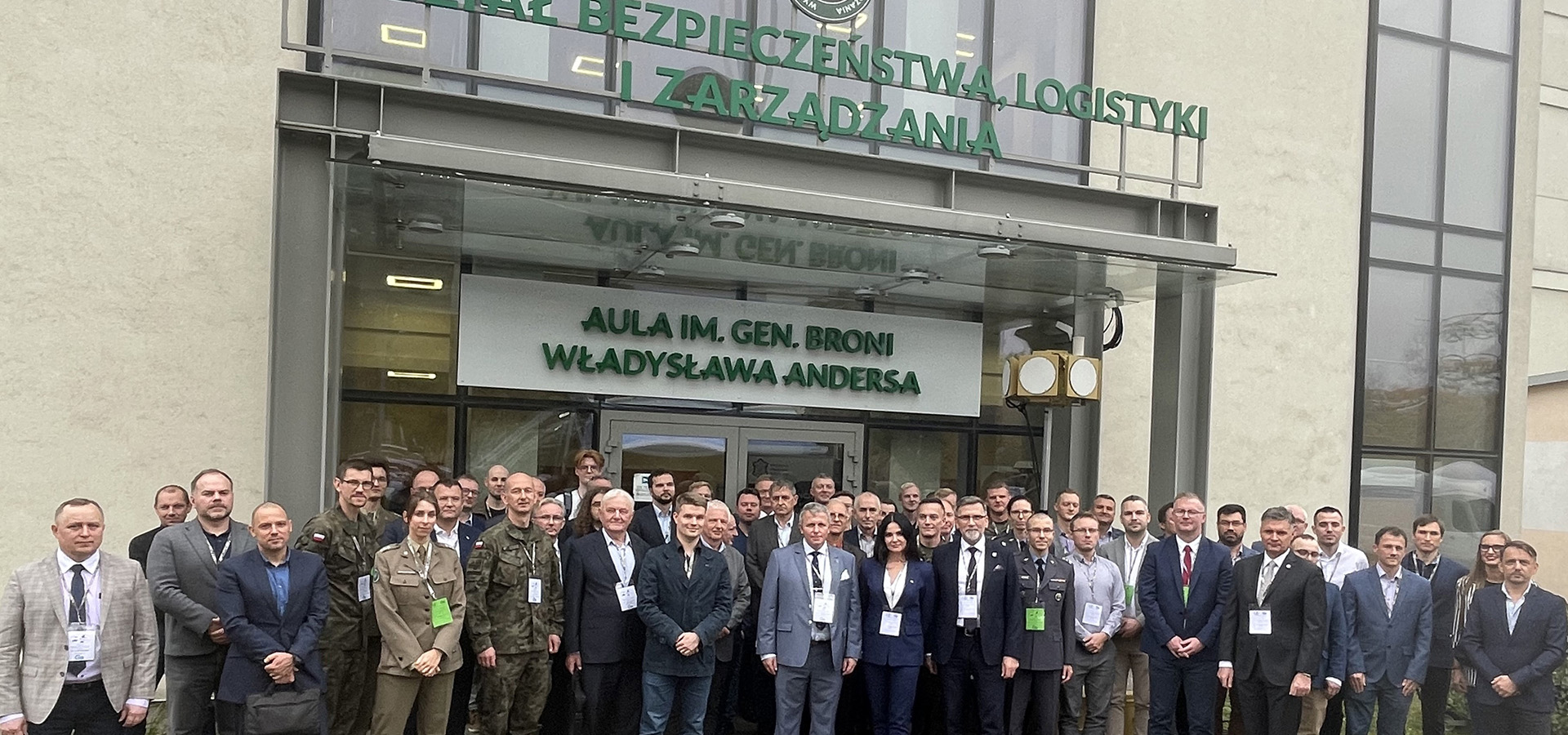 Fot. 2. Uczestnicy konferencji stojacy tyłem do budynku, pozujący do wspólnego zdjęcia.