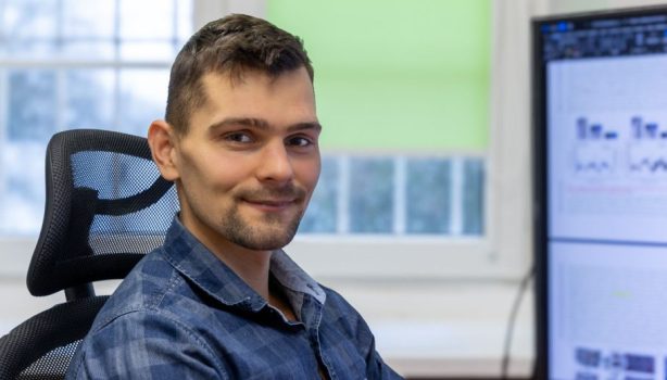 Naukowiec z WIM WAT, Michał Kucewicz, siedzący w fotelu przed biurkiem z komputerem, głowa skierowana do aparatu.