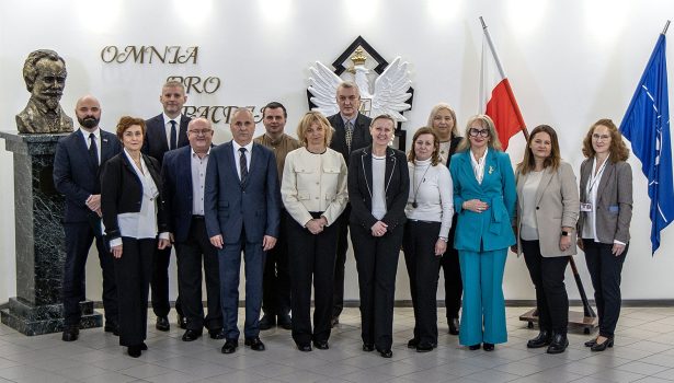 Przedstawiciele szkół i WAT - grupowe zdjęcie, osoby stoją obok siebie, w tle flaga Polski, Nato oraz Godło