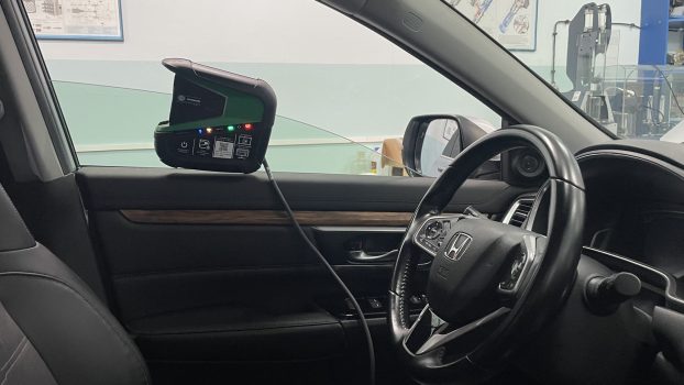 Tester Mega Macs X zawieszony na uchylonej szybie przedniej, podłączony do gniazda diagnostycznego OBD II samochodu