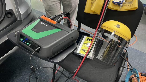 „Przystawka pomiarowa do testera Mega Macs X umożliwiająca wykonywanie pomiarów niskiego (do 60 V) oraz wysokiego (do 1000 V) napięcia, po prawej stronie elementy odzieży ochronnej (rękawice elektroizolacyjne, przyłbica) oraz tabliczki ostrzegawcze przydatne przy pracach przy samochodach z napędem elektrycznym i hybrydowym