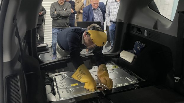 Na pierwszym planie pan Łukasz Żelazo odłączający zworę serwisową akumulatora wysokiego napięcia, na dalszym planie nauczyciele akademiccy uczestniczący w szkoleniu obserwujący pokaz.