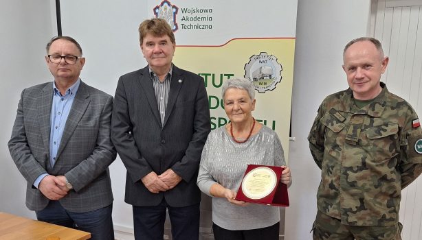 Mgr Wiesława Zielnik stojąca wraz z dyrekcją Instytutu Pojazdów i Transportu oraz kierownikiem Zakładu Materiałów Pędnych i Smarów – zdjęcie pamiątkowe wykonane na zakończenie spotkania, w tle rollup z nazwą i logo instytutu