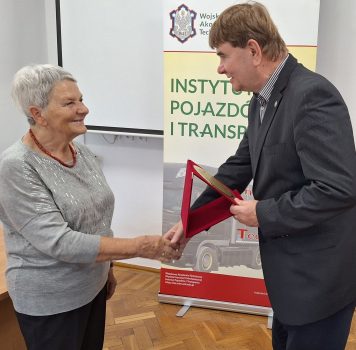 Dyrektor Instytutu Pojazdów i Transportu doktor habilitowany inżynier Mirosław Gidlewski wręczający okolicznościową paterę pani Wiesławie Zielnik, na dalszym planie rollup z nazwą i logo instytutu