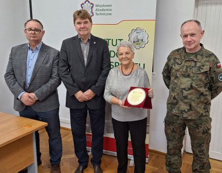 Mgr Wiesława Zielnik stojąca wraz z dyrekcją Instytutu Pojazdów i Transportu oraz kierownikiem Zakładu Materiałów Pędnych i Smarów – zdjęcie pamiątkowe wykonane na zakończenie spotkania, w tle rollup z nazwą i logo instytutu