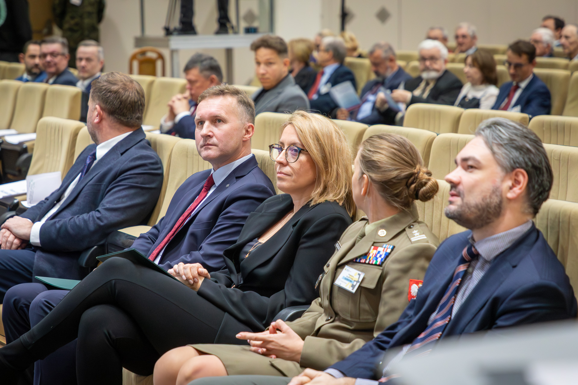 Przedstawiciele organizatorów na Konferencji. Siedzą w fotelach w sali klubu WAT, przodem do prowadzących i ekranu.