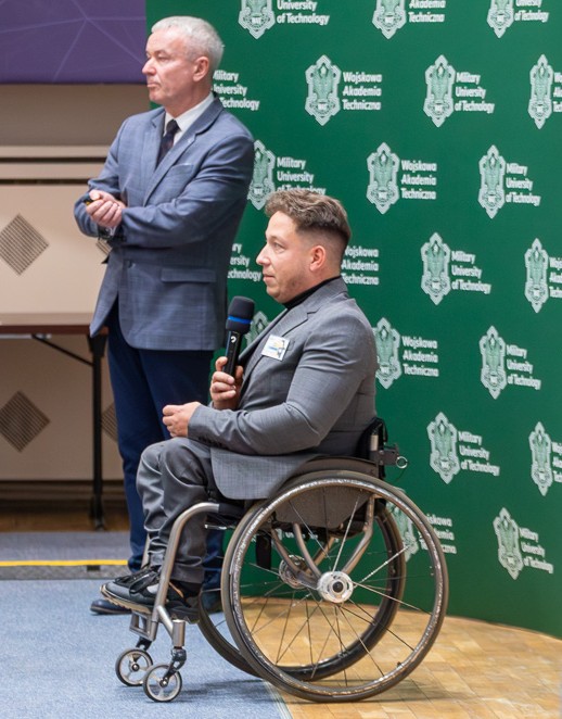 Panowie Tomasz Matuszewski, Sekretarz Mazowieckiej Rady Bezpieczeństwa Ruchu Drogowego (stoi) oraz Pan Artur Świercz, Pełnomocnik Zarządu Województwa Mazowieckiego ds. Osób Niepełnosprawnych (siedzi na wózku inwalidzkim).