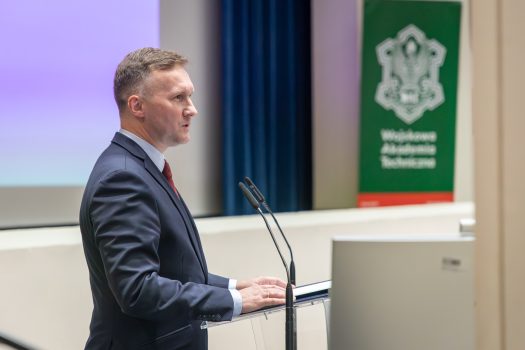 Prof. dr hab. inż. Janusz Bogusz, Prorektor ds. naukowych WAT podczas sesji otwierającej Konferencję; stoi przodem do zgromadzonych gości przy mównicy.