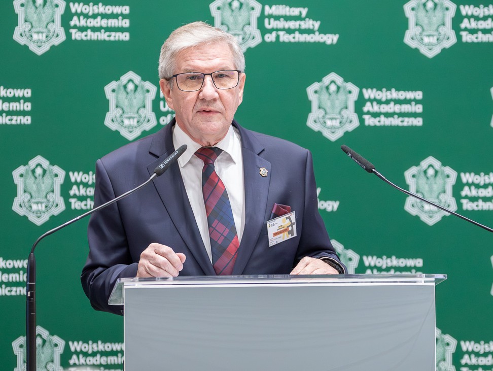 Prof. Jerzy Jackowski, Dziekan WIM, Kierownik Centrum Wiedzy o Dostępności WAT zabiera głos podczas sesji otwierającej Konferencję; stoi przodem do zgromadzonych gości przy mównicy.
