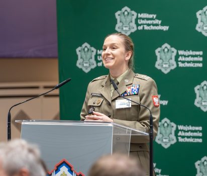 Ppłk. dr inż. Katarzyna Rzadkowska, Dyrektor Centrum Weterana działań poza granicami Państwa z MON, stoi przy mównicy, przodem do gości, w tle baner WAT.