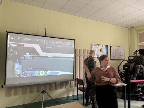 Prezentacja symulatora VR jazdy samochodem ciężarowym. Przy projektorze stoi p. Olga Gajda.