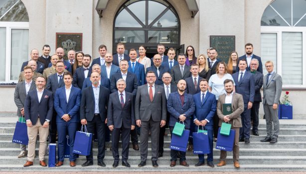 Grupa osób stojąca przed budynkiem, pozując do zdjęcia, stoją w kilku szeregach.