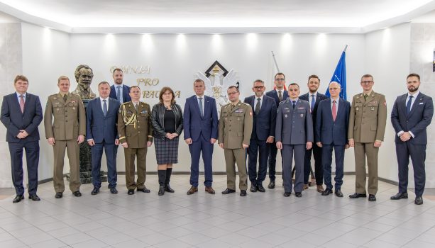 Grupa osób pozująca do zdjęcia, osoby stoją obok siebie w szeregu. Osoby ubrane elegancko, a wojskowi w mundurach.