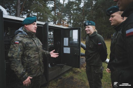 Podchorążowie stoją przy agregacie pompowym na dworzu.