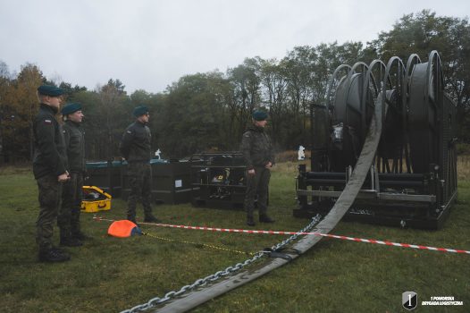 Podchorąży stojący przy rurociągu przeprawowym wraz z nawijarką.