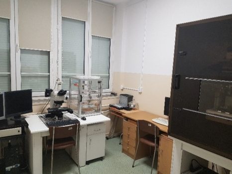 Widok pomieszczenia, na wprost i po prawej szafki, biurko, urządzenia laboratoryjne.
