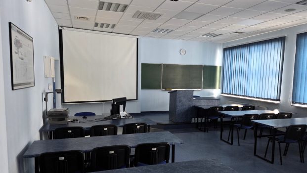 Sala wykładowa, zdjęcie przodem do tablicy, widoczne ławki i krzesła.
