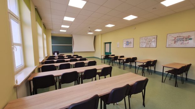 Sala wykładowa, zdjęcie przodem do tablicy, widoczne ławki i krzesła.