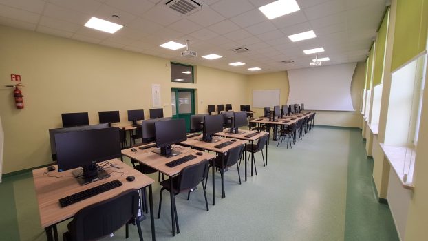 Pracownia komputerowa. Na środku wzdłuż sali stoją stoły z komputerami, monitorami itp.