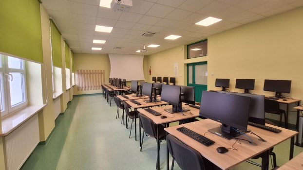 Pracownia komputerowa. Na środku wzdłuż sali stoją stoły z komputerami, monitorami itp.