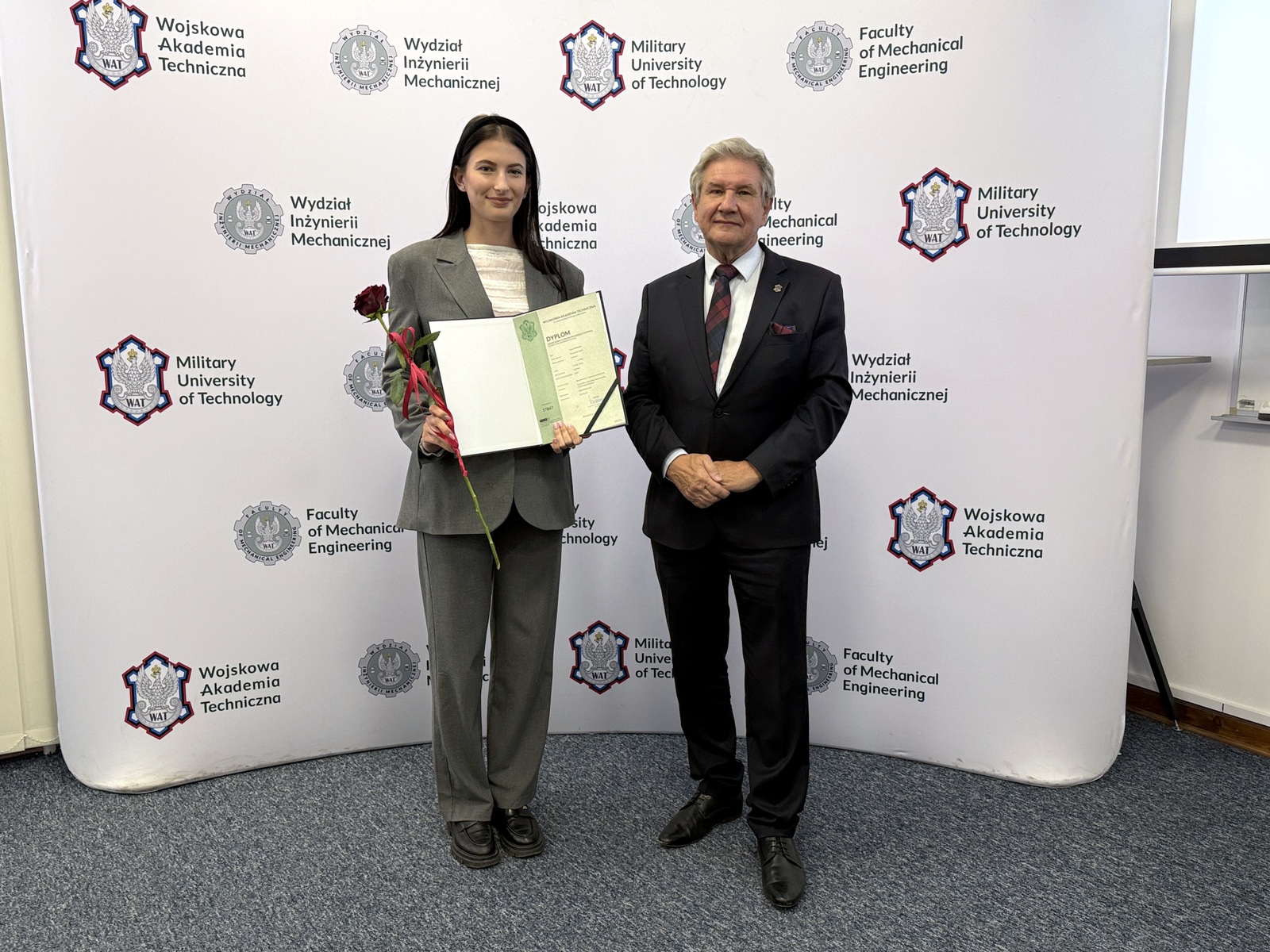 Dziekan wraz ze studentką trzymającą wyróżnienie, w tle ścianka z logami WAT i WIM