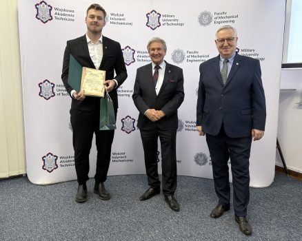 Dziekan oraz Kierownik Dziekanatu wraz ze studentem trzymającym wyróżnienie, w tle ścianka z logami WAT i WIM