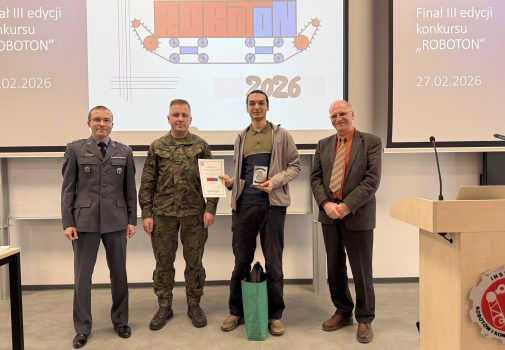 Na tle baneru z napisem ROBOTON stoją: sekretarz komisji konkursowej, Prorektor ds. Wojskowych, laureat nagrody Rektora WAT trzymający dyplom i statuetkę oraz kierownik IRiKM WIM WAT. Wszyscy uśmiechają się do zdjęcia.