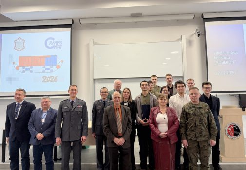 Na tle baneru ROBOTON stoi grupa przedstawicieli komisji konkursowej i uczestników konkursu. Wszyscy są ubrani odświętnie i uśmiechają się do zdjęcia.