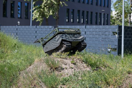 Robot gąsienicowy pokonuje trawiaste wzniesienie, tracąc kontakt z podłożem przy przejeździe przez jego szczyt.