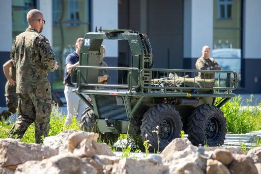 Robot kołowy porusza się po gruzowisku, za nim idzie żołnierz-operator.