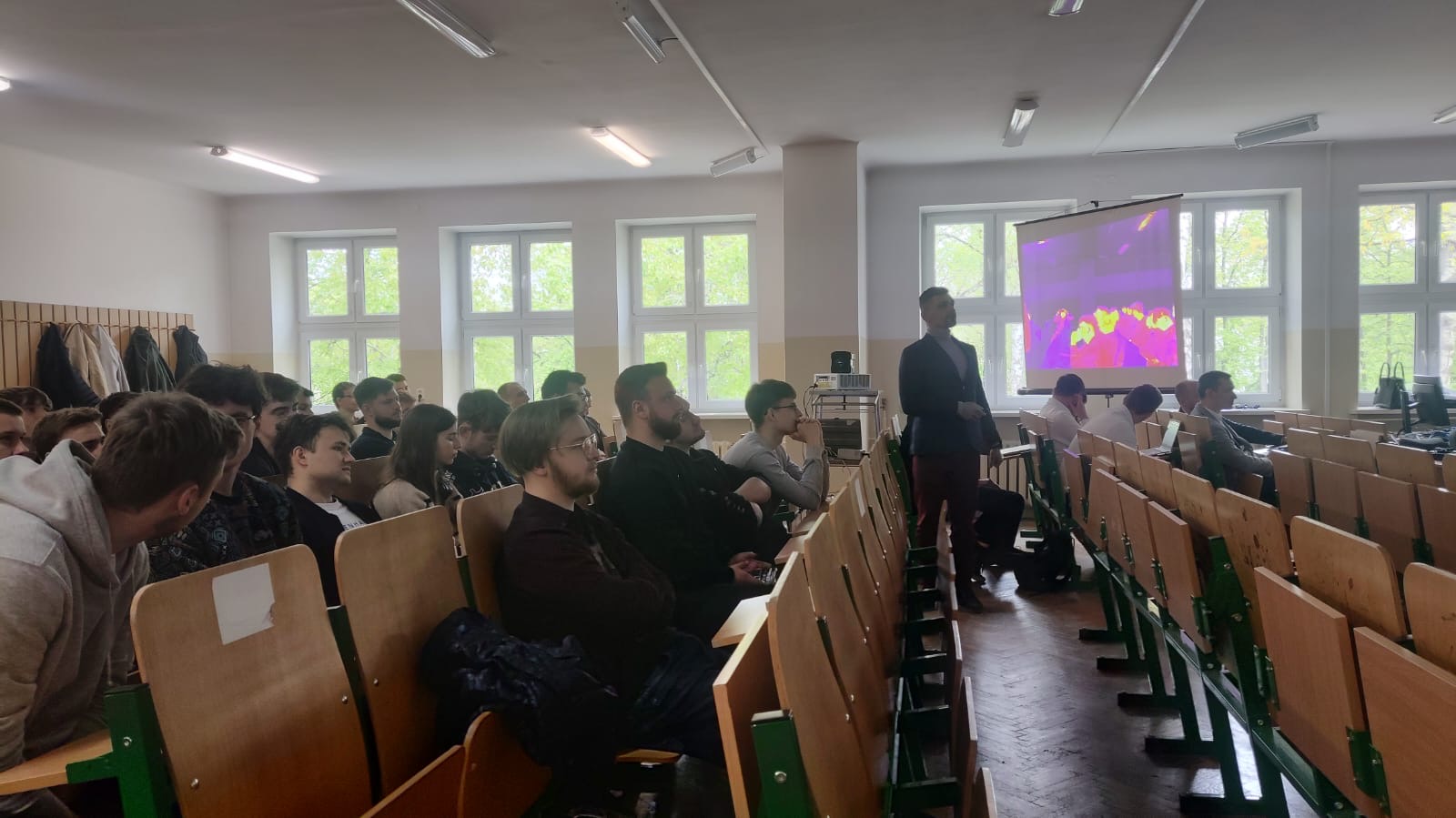 Studenci siedzący w sali wykładowej, słuchający pracownika naukowego WIM, zachęcajacego do wyboru specjalności w IMiIO.