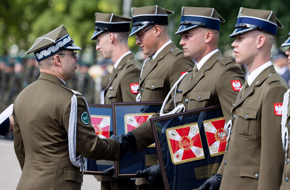 Oficerowie na placu manewrowym WAT. W rzędzie bokiem do zdjęcia stoją młodzi oficerowie. Rektor ściska dłoń jednemu z nich.