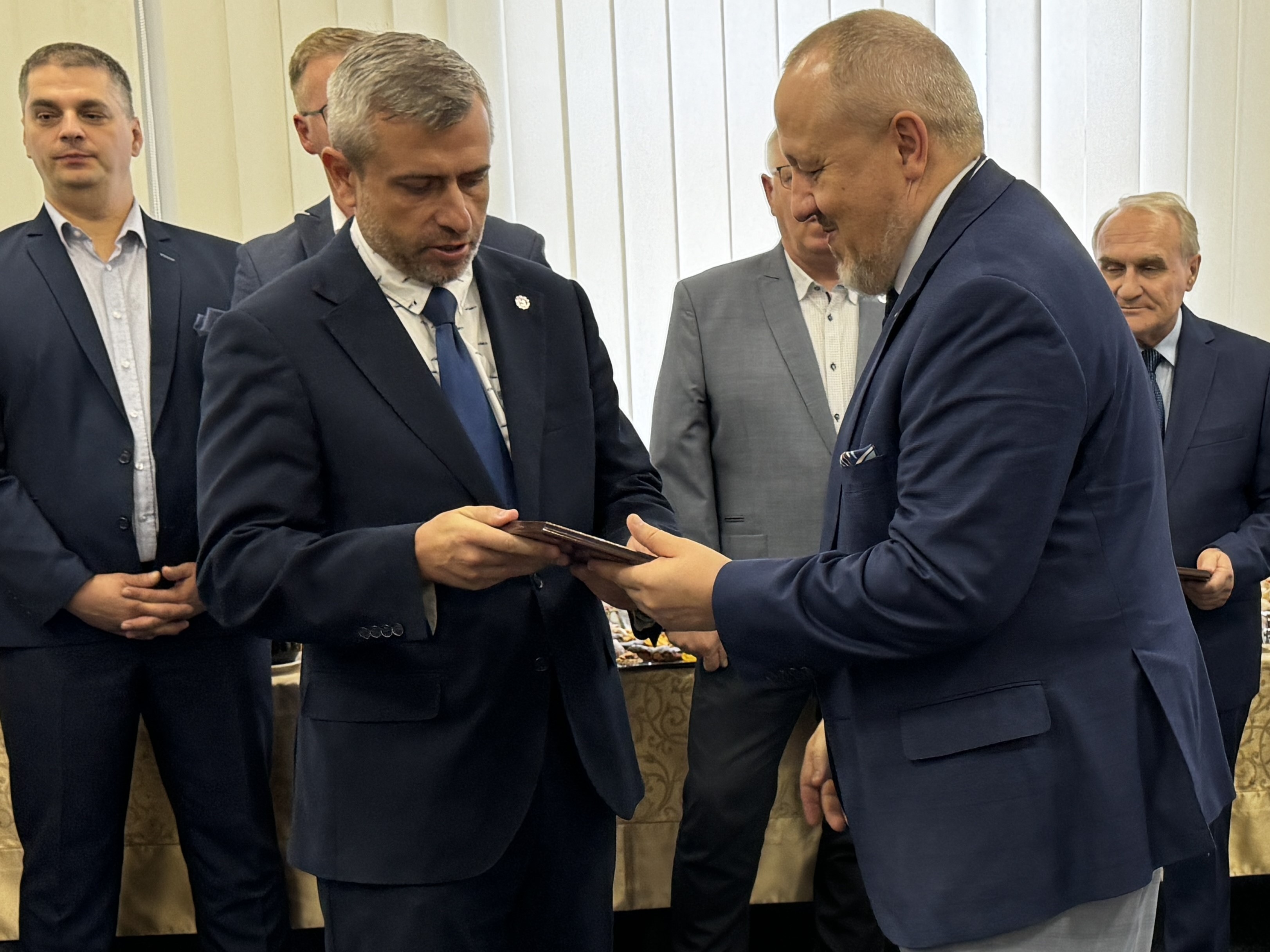 Dziekan J.Małachowski dziękuje i wręcza pamiątkowy ryngraf dr. P.Szurgottowi, w tle kilka osób, z tyłu baner WIM WAT.