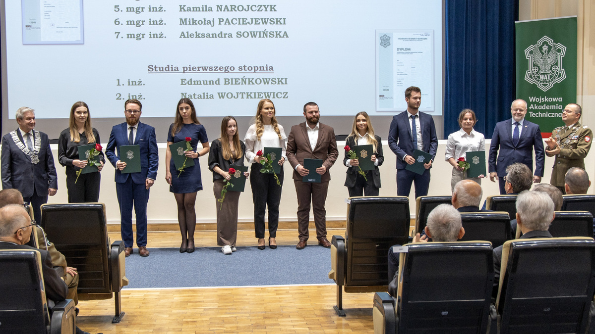 Tyłem do sceny, przodem do zgromadzonych stoją wyróżnione osoby.