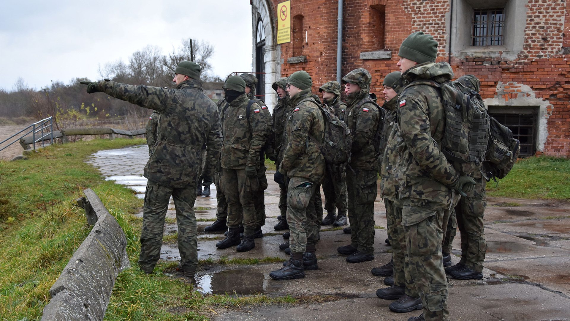 Podchorążowie na szkoleniu z organizowania przepraw; grupa podchorążych stojących tyłem do budynku.