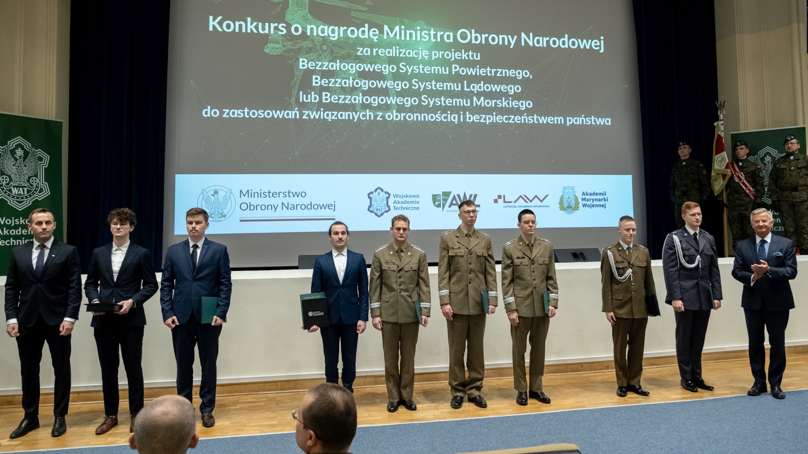 Grupa osób wyróznionych w konkursie, laureaci stoją obok siebie w sali kinowej WAT, przodem do zgromadzonych gości.