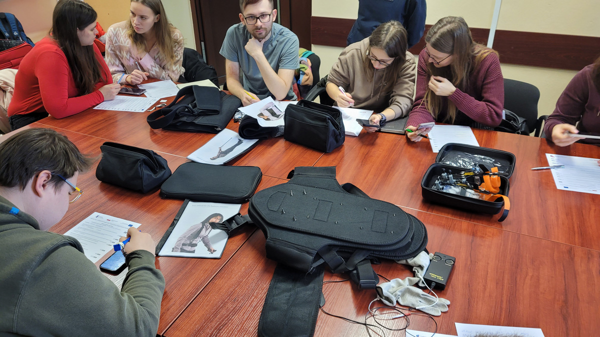 5. Grupa studentów przy stole z różnego rodzaju demonstratorami symulowania ograniczeń ruchu i funkcji motorycznych człowieka.