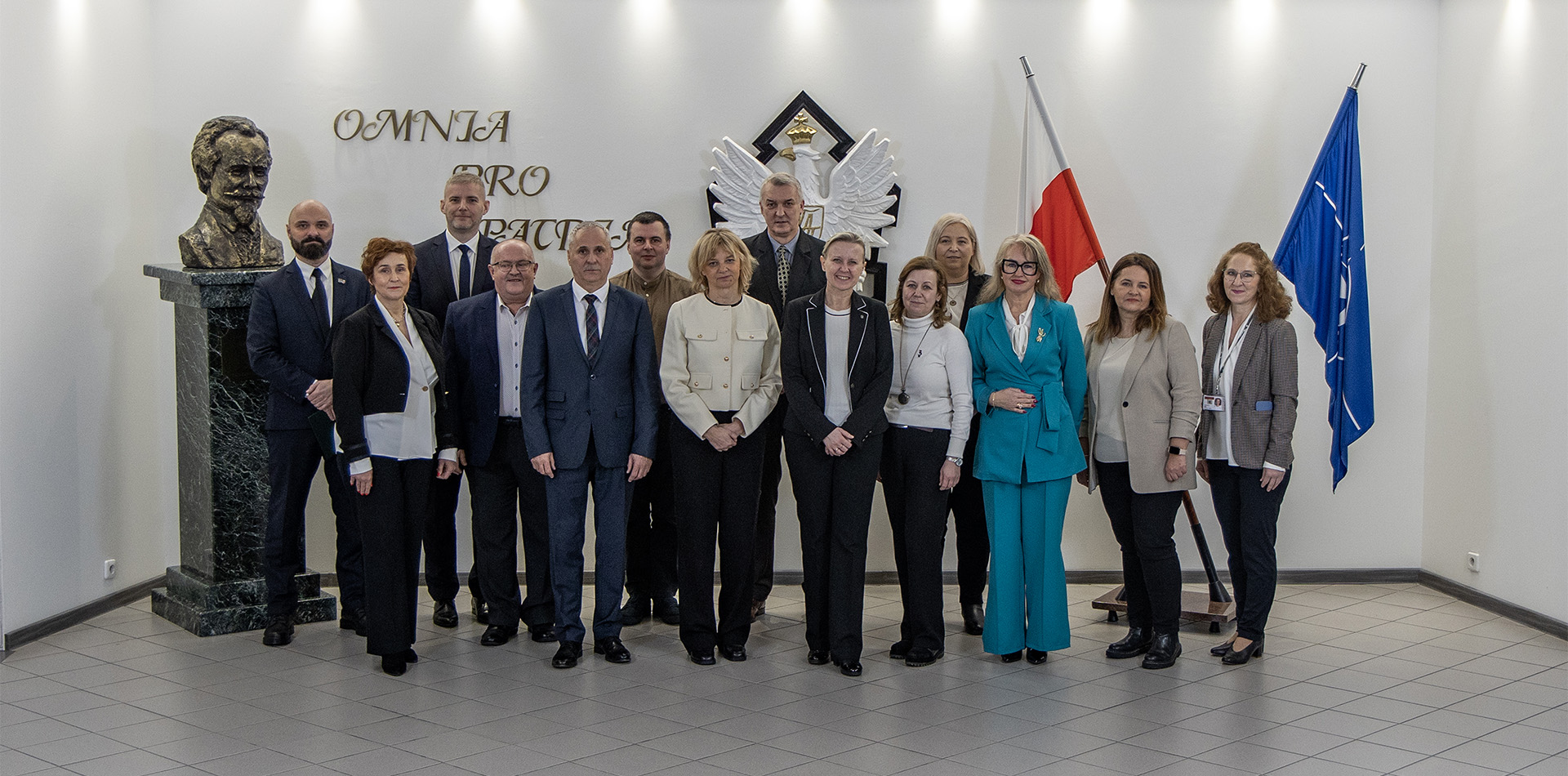 1. Przedstawiciele szkół i WAT - grupowe zdjęcie, osoby stoją obok siebie, w tle flaga Polski, Nato oraz Godło.