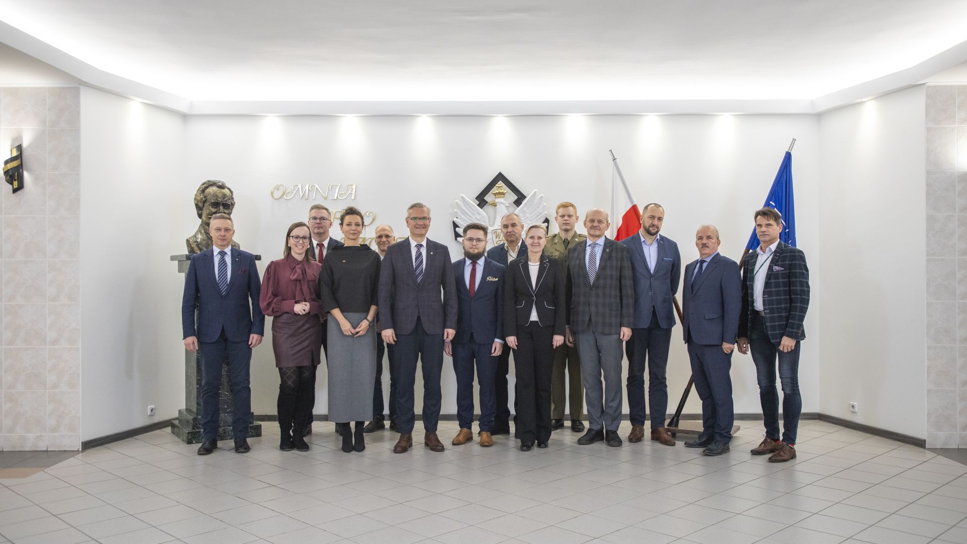 Uczestnicy spotkania pozują do pamiatkowego zdjecia, stoją obok siebie przodem do fotografa.